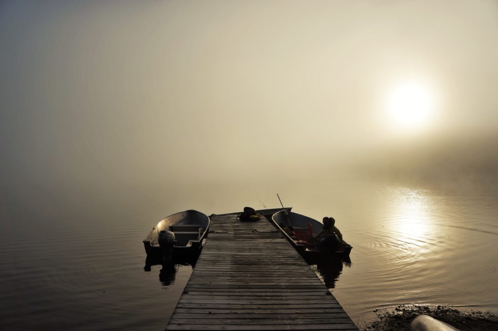 Boats tied to a dock on a lake in the mist during sunrise